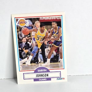 May include: A basketball trading card featuring Earvin Johnson in a Los Angeles Lakers uniform, number 32. The card has a white border with blue and red accents. The card is from the Fleer '90 collection.