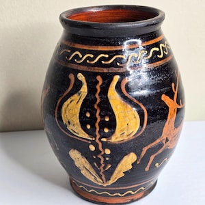May include: A black ceramic vase with a glossy finish, featuring hand-painted yellow and orange floral motifs and a deer silhouette. The vessel has a wide, rounded body, a thick rim, and decorative wavy line patterns encircling the top and base.