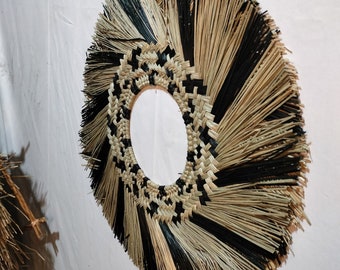 Puede incluir: Un gran tapiz de pared redondo hecho de fibras naturales tejidas. Las fibras están dispuestas en un patrón circular con hebras alternas de color negro y natural. El centro del tapiz es un círculo grande y abierto.