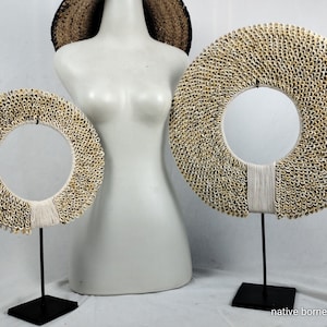 May include: Two decorative necklaces made of white seashells on black stands. The necklaces are round and have a hole in the center. The text "native borneo papua" is at the bottom of the image.