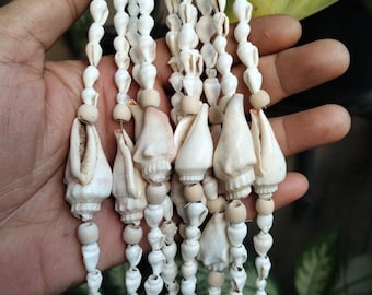 May include: A collection of hanging strands featuring small white seashells and larger, smooth, off-white conch-like shells interspersed with light tan wooden beads. The text "native borneo papua" is printed in white in the bottom right corner.