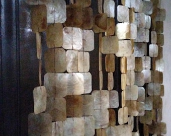 May include: A decorative curtain made of square and rectangular shell pieces in shades of brown, beige, and white. The shells are strung together, creating a textured, natural look. The text "Native Borneo Papua" is visible.