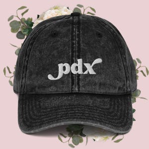 Könnte beinhalten: Eine schwarze, abgenutzte Baseballkappe aus Denim mit einem weißen gestickten Logo, auf dem "pdx" steht.