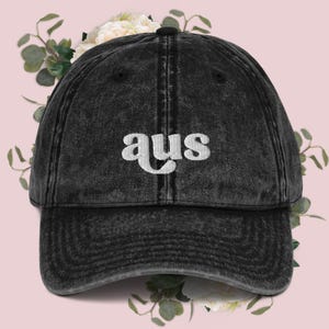 May include: A black distressed denim baseball cap with white embroidered text that reads "aus".