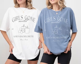 Puede incluir: Dos mujeres con camisetas blancas y azules con el texto "Girls Gone Mild" y un gráfico de velas y flores. El texto "Kate's Bachelorette" también está en las camisetas.