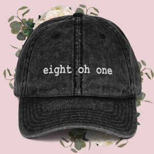 May include: A black distressed denim baseball cap with white embroidered text that reads "eight oh one".
