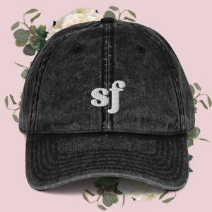 Op de afbeelding: Een zwarte baseballcap in vintage stijl met een wit geborduurd "sf" logo.