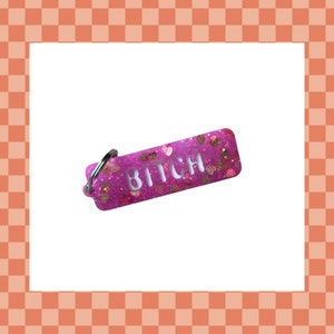 May include: Pink keychain with glitter and the word "BITCH" in white letters.