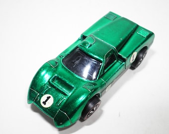 May include: A green toy car with black wheels and a number "1" on the side. The car is a vintage Hot Wheels model.