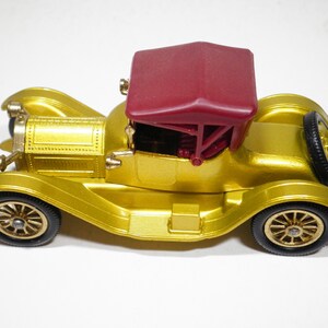 May include: A gold toy car with a red convertible top. The car has a detailed design and is a vintage style.