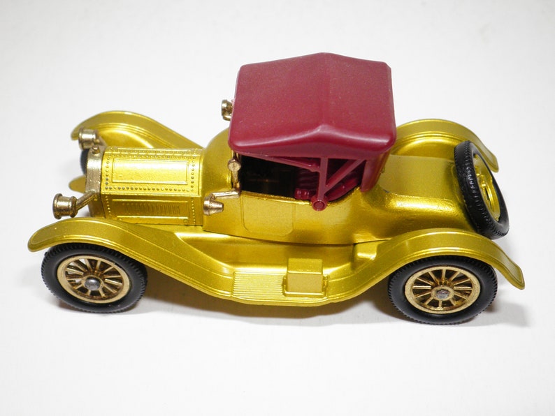 May include: A gold toy car with a red convertible top. The car has a detailed design and is a vintage style.