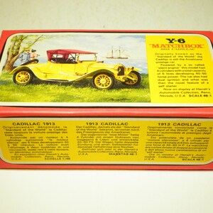 May include: A yellow 1913 Cadillac toy car model in a red box with a white and yellow label. The box features text in English, French, German, and Italian describing the car's history and features. The text on the box reads "Y-6 Matchbox 1913 Cadillac".