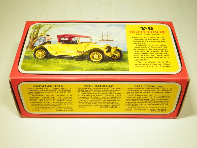 May include: A yellow 1913 Cadillac toy car model in a red box with a white and yellow label. The box features text in English, French, German, and Italian describing the car's history and features. The text on the box reads "Y-6 Matchbox 1913 Cadillac".
