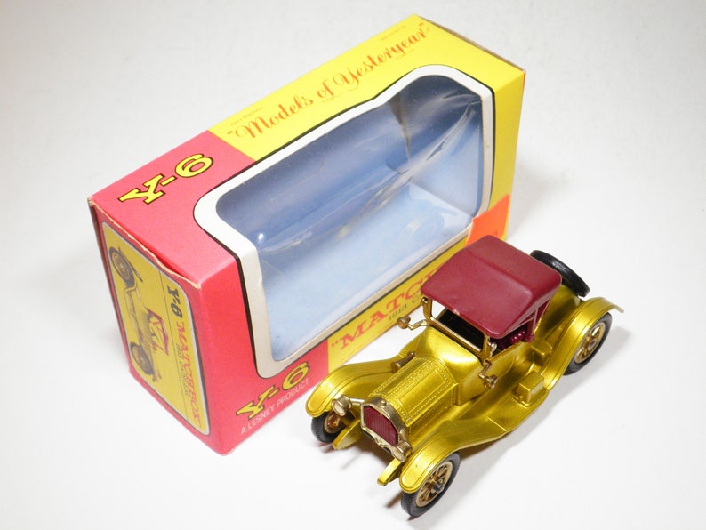 May include: A gold toy car with a red roof in its original box. The box is red and yellow and says "Models of Yesteryear" and "Matchbox" on it.