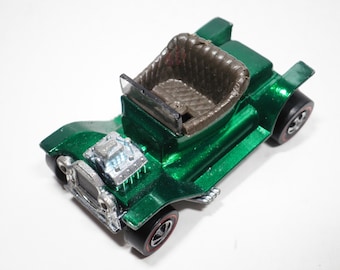 May include: A green toy car with a brown leather seat and a chrome engine. The car has a black windshield and black wheels with red tires.