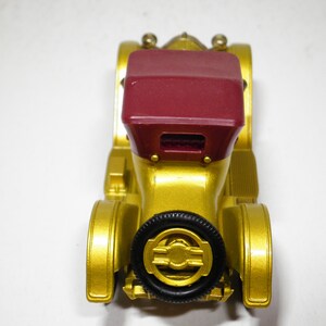 May include: A gold toy car with a red convertible top. The car has black wheels and a detailed design.