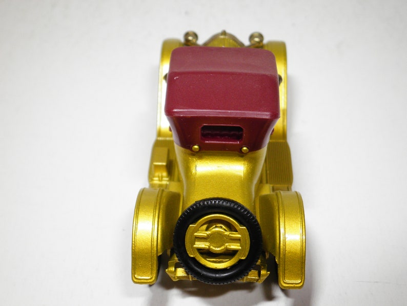 May include: A gold toy car with a red convertible top. The car has black wheels and a detailed design.