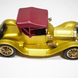 May include: A gold toy car with a red convertible top. The car has a detailed design and black wheels.