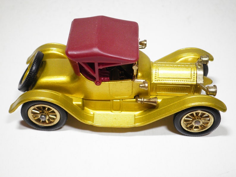 May include: A gold toy car with a red convertible top. The car has a detailed design and black wheels.