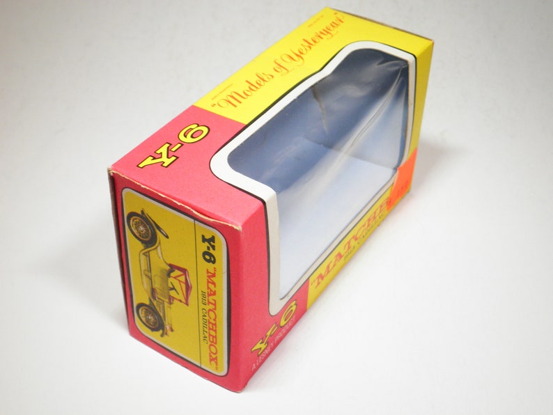 May include: A red and yellow Matchbox toy car box with a clear plastic window showing a 1913 Cadillac. The box has the text "Y-6" and "Matchbox" on it.