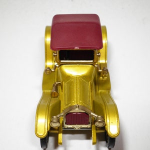 May include: A gold toy car with a maroon roof. The car has a detailed front grill and headlights.