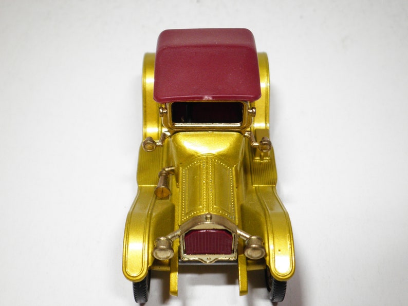May include: A gold toy car with a maroon roof. The car has a detailed front grill and headlights.