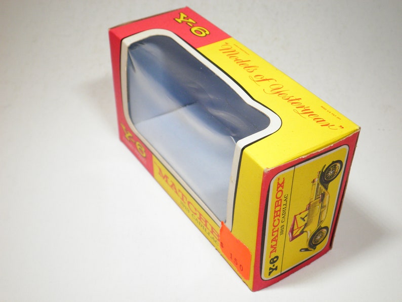 May include: A yellow and red cardboard box with a clear plastic window showing a toy car. The box has the text "Y-6 Matchbox Models of Yesteryear" and "1913 Cadillac" printed on it.