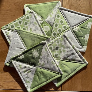Puede incluir: Conjunto de cinco posavasos de tela verde y blanca con una variedad de patrones, incluyendo regaderas, hojas y diseños geométricos.