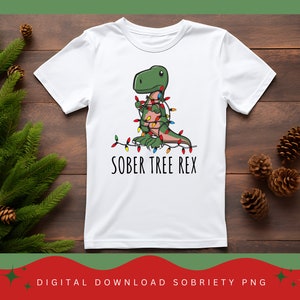 May include: White t-shirt with a green dinosaur wrapped in Christmas lights and the text "SOBER TREE REX".