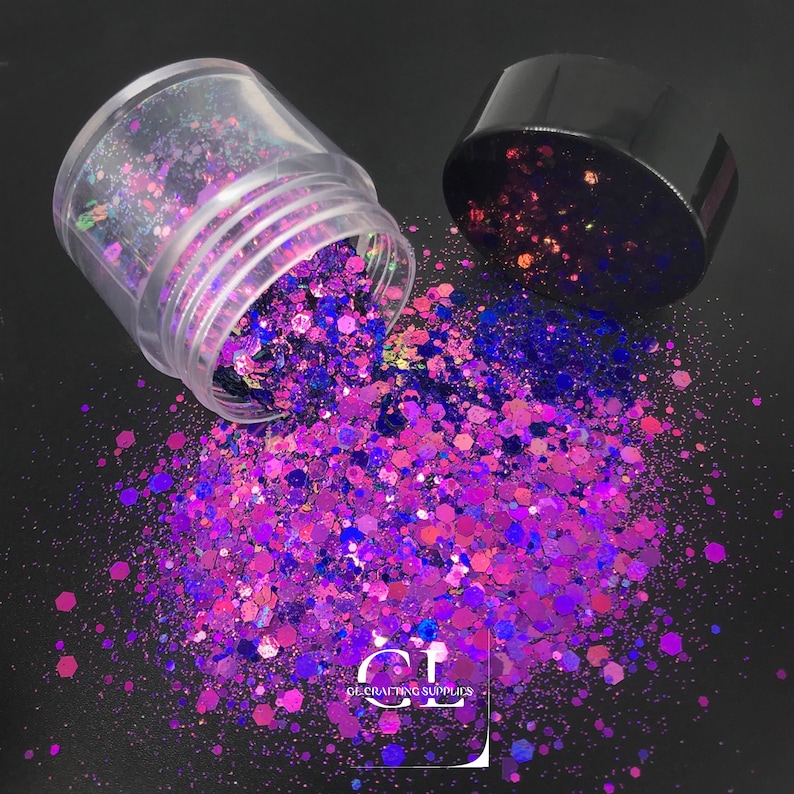 Puede incluir: Un tarro de pl&aacute;stico transparente con tapa negra, volcado, derramando una vibrante mezcla de purpurina morada, rosa y azul. La purpurina tiene varias formas y tama&ntilde;os, creando un efecto brillante. La imagen est&aacute; sobre una superficie negra.