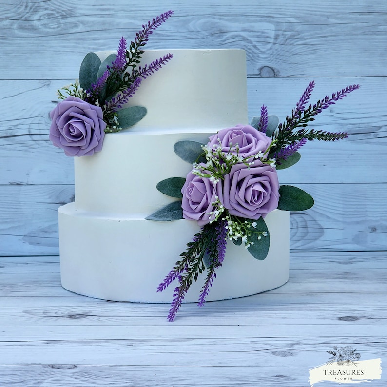 May include: A three-tiered white wedding cake decorated with purple roses and lavender sprigs.