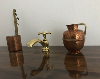 May include: Three decorative items made of copper and brass. A small copper pitcher with a hammered finish and a brass handle. A small copper cup with a brass handle. A brass faucet with a cross-shaped handle.