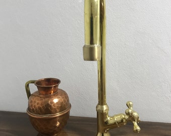 May include: A gold-toned faucet with a curved spout and a cross-shaped handle. The faucet is on a wooden surface next to a copper pitcher.