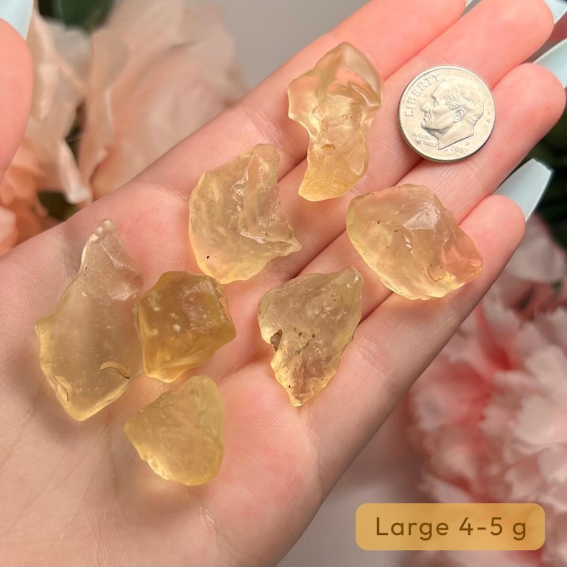 Puede incluir: Una colecci&oacute;n de piedras preciosas en bruto transl&uacute;cidas de color amarillo-naranja, con una moneda para comparar el tama&ntilde;o. Las piedras tienen forma irregular y parecen ser cristales naturales. El texto de la imagen dice "Large 4-5 g".