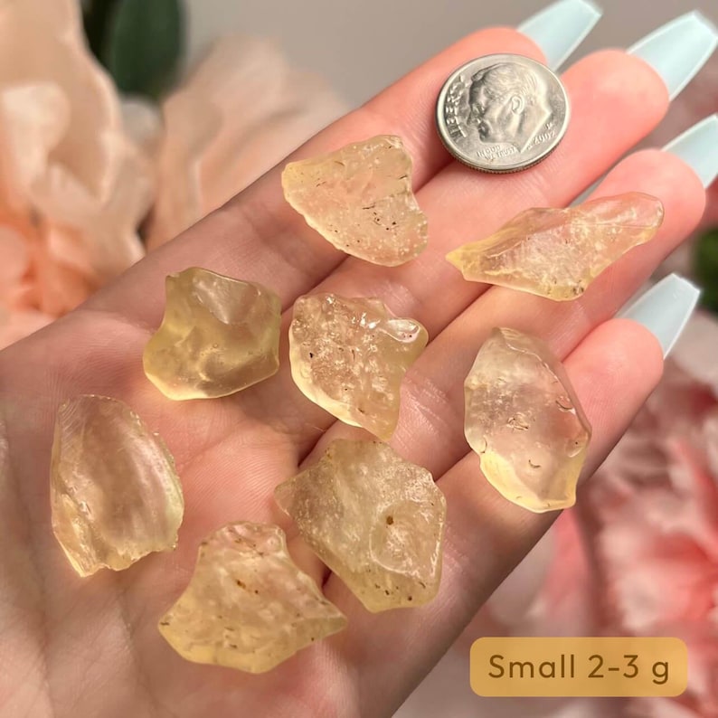 Puede incluir: Se muestra una colecci&oacute;n de peque&ntilde;os cristales transl&uacute;cidos de color amarillo-naranja, cada uno con una forma &uacute;nica. Se incluye una moneda de diez centavos estadounidense como referencia de tama&ntilde;o. Los cristales est&aacute;n etiquetados como "Small 2-3 g".