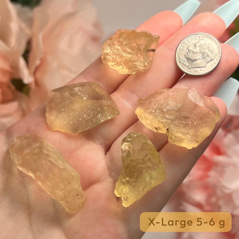 Puede incluir: Una mano sostiene varios cristales en bruto transl&uacute;cidos de color amarillo-naranja, con una moneda de diez centavos estadounidense para comparar el tama&ntilde;o. Los cristales tienen forma irregular y var&iacute;an en tama&ntilde;o. El texto "X-Large 5-6 g" est&aacute; en un recuadro amarillo.