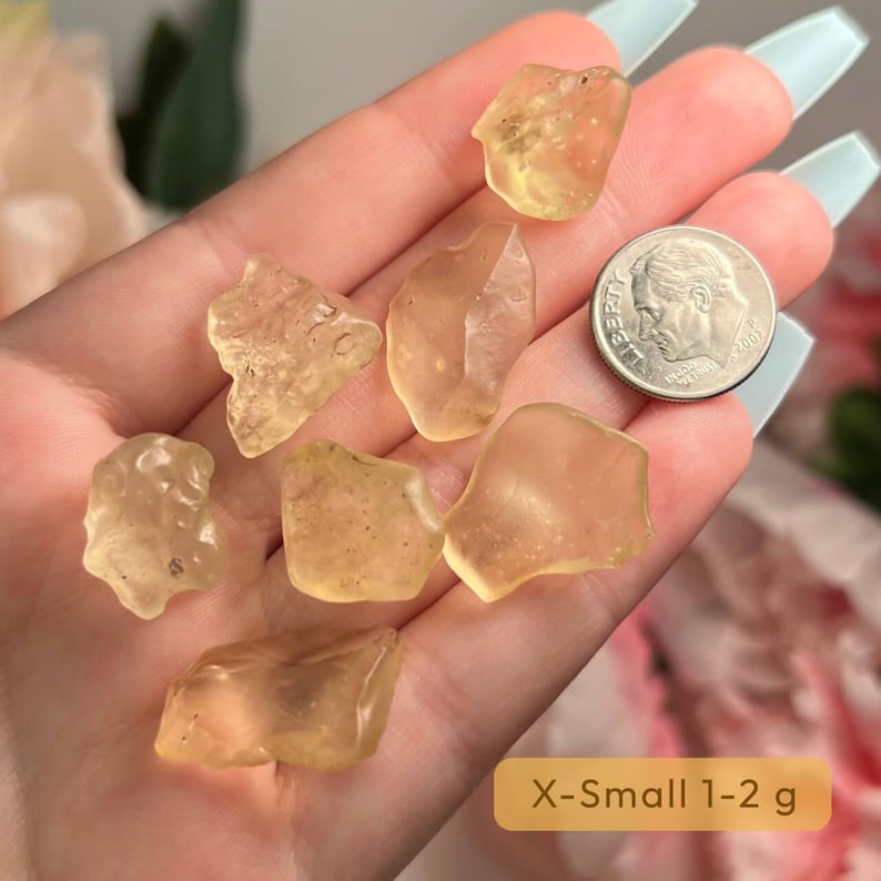 Puede incluir: Una colecci&oacute;n de peque&ntilde;as piedras en bruto transl&uacute;cidas de color &aacute;mbar. Las piedras tienen formas irregulares y tama&ntilde;os variables. Se incluye una moneda para comparar el tama&ntilde;o. La imagen incluye el texto "X-Small 1-2 g".