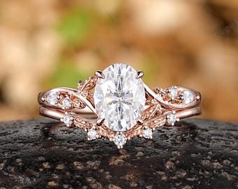 May include: Rose gold engagement ring with a large oval-cut center stone and smaller accent stones. The ring features a delicate, floral-inspired design. The band is also adorned with small, sparkling stones.
