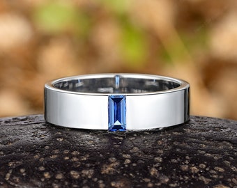 May include: A silver band with a rectangular blue sapphire gemstone set in the center.