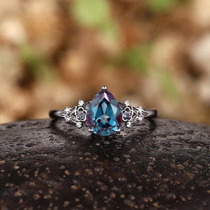 May include: A pear-shaped, blue and purple gemstone ring with a silver band and delicate floral accents.