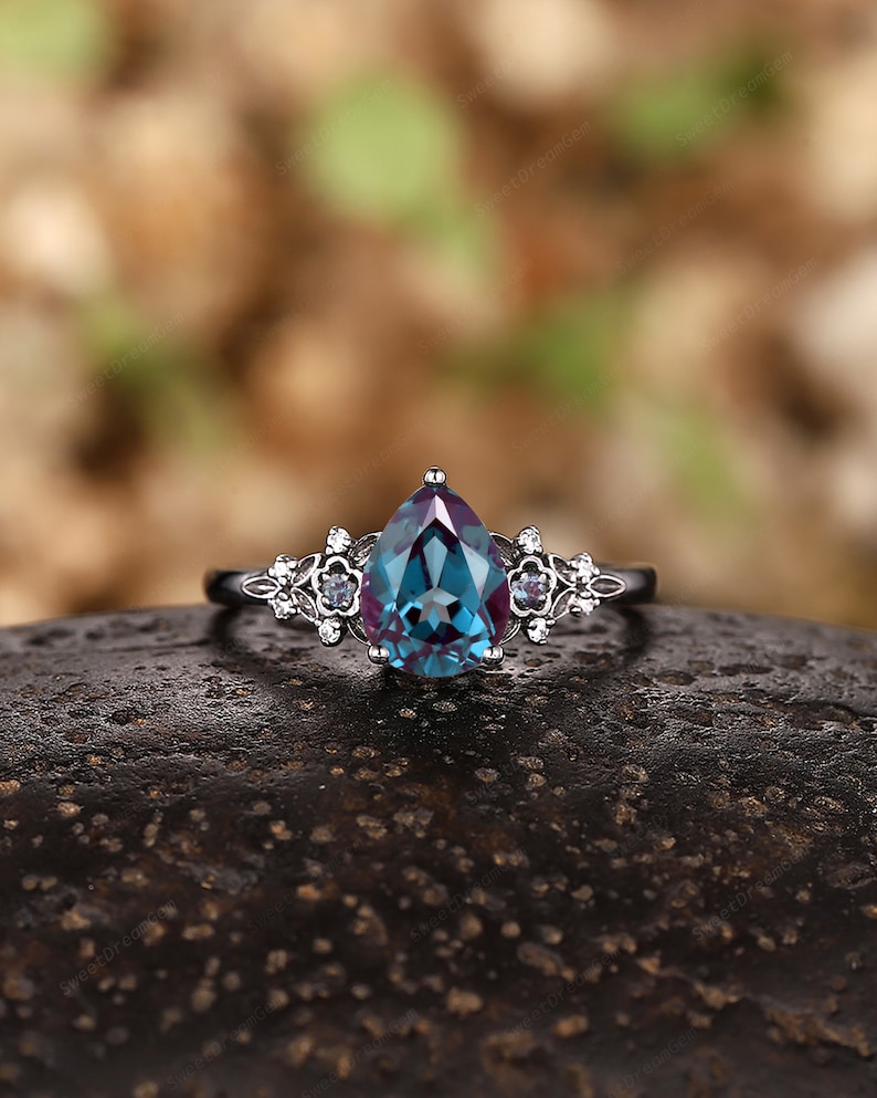 May include: A pear-shaped, blue and purple gemstone ring with a silver band and delicate floral accents.