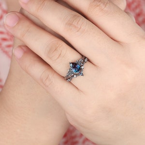 May include: A pear-shaped blue gemstone ring with a black metal setting and a delicate floral design. The ring is set on a white band.