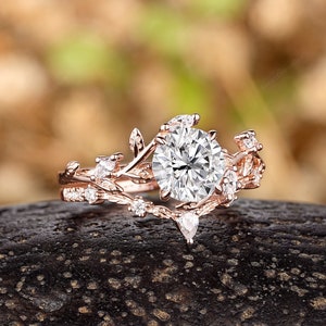 May include: A rose gold engagement ring with a large round center stone and smaller accent stones set in a delicate leaf design.