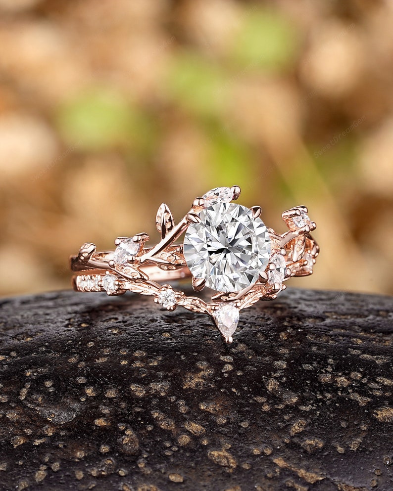 May include: A rose gold engagement ring with a large round center stone and smaller accent stones set in a delicate leaf design.