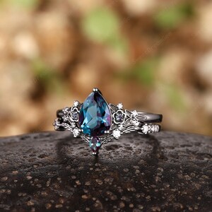 May include: A pear-shaped, blue-green gemstone ring with a black metal band and a delicate floral design. The ring is set with smaller white gemstones and a single, smaller blue-green gemstone.