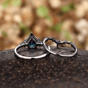 May include: A pair of silver rings featuring a pear-shaped blue gemstone and smaller clear gemstones. The rings are displayed on a dark brown surface.
