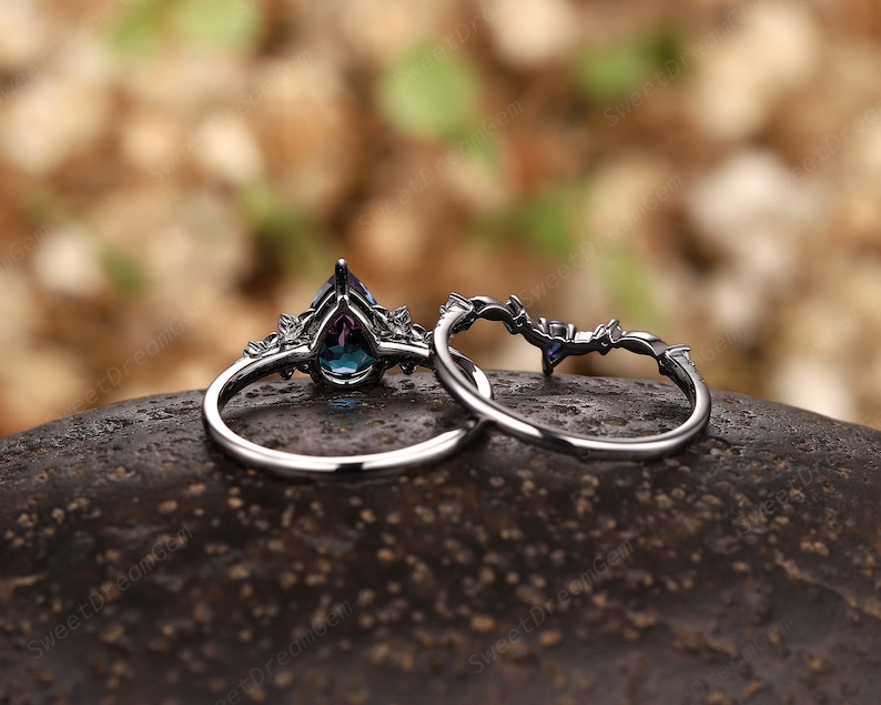 May include: A pair of silver rings featuring a pear-shaped blue gemstone and smaller clear gemstones. The rings are displayed on a dark brown surface.