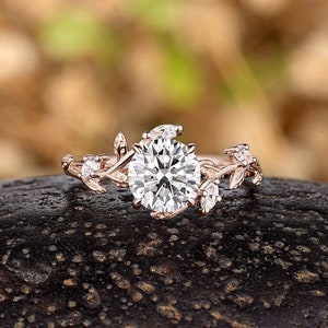 May include: A rose gold engagement ring with a large round center stone and smaller stones set in a delicate leaf design.
