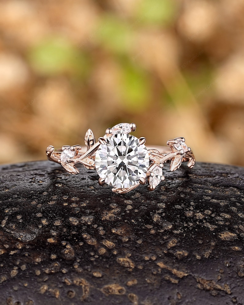 May include: A rose gold engagement ring with a large round center stone and smaller stones set in a delicate leaf design.