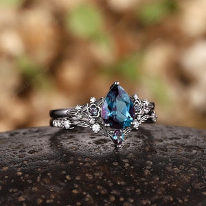 May include: A pear-shaped, blue-green gemstone ring with a silver band and a delicate floral design. The ring is set with smaller white gemstones.